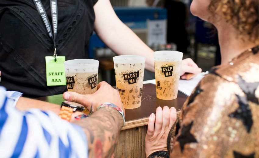 Bild zeigt zwei Personen an einer Bar, vor ihnen sind drei Hartplastikbecher am Tresen mit der Aufschrift "Keep me" und "Reuse me". (c) Globelet Reusable auf Unsplash