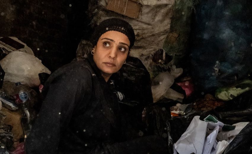 Bild zeigt eine Frau in schwarzer Kleidung vor einem Berg aus alter Textilien. (c) Ingmar Ostermaier)